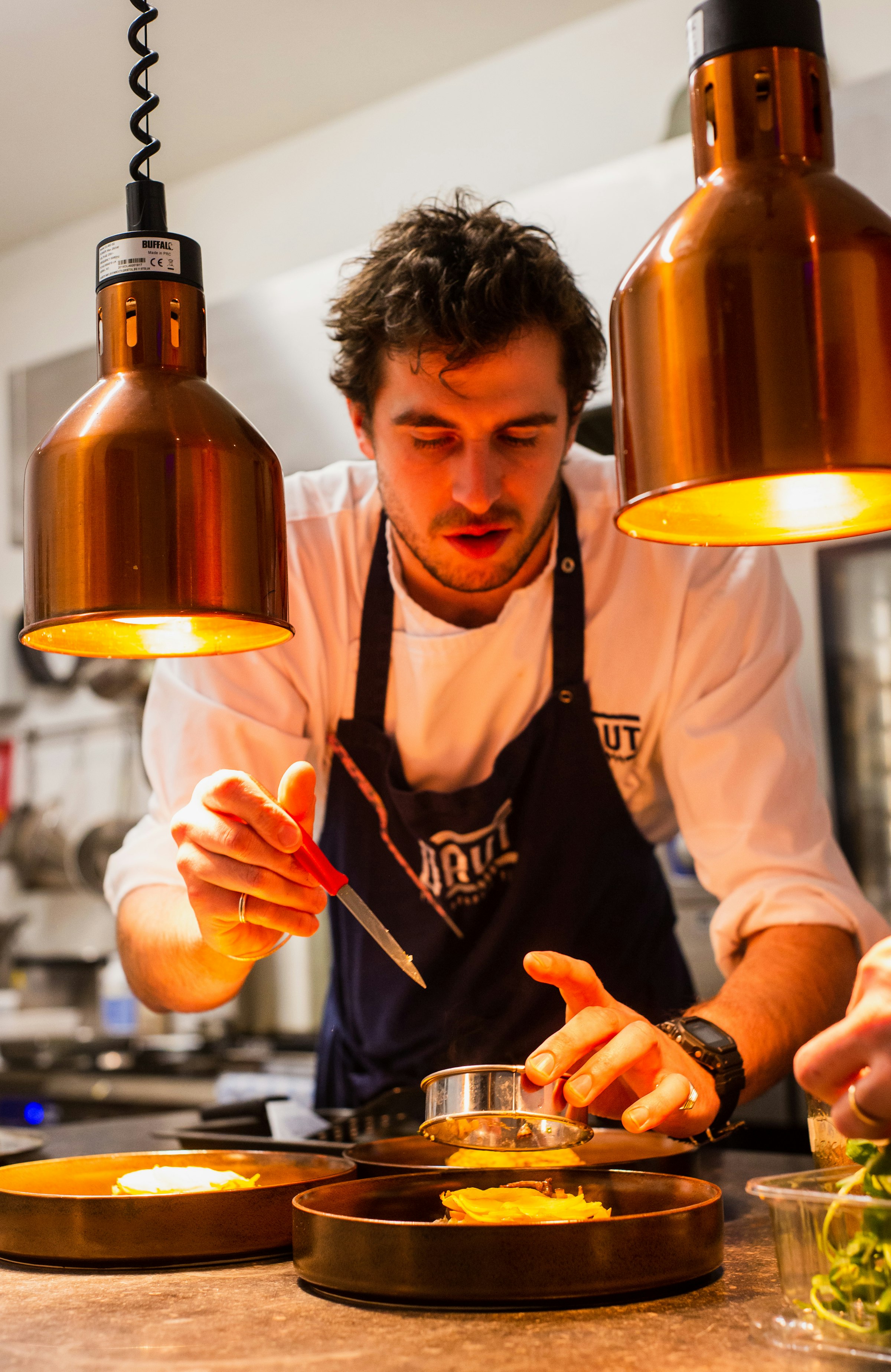 Chef plating dishes under commercial heat lamps